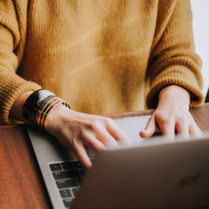 Frau auf Macbook mit Armbändern am Arbeiten